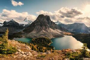 montar Assiniboine con rayos de sol y azul claro lago en otoño pino bosque foto