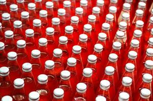 Red juice bottles with screw cap in conveyor belt at beverage processing plant photo