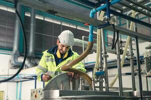 Caucasian technician engineer man in uniform with tablet checking and control boiler tanks and liquid pipeline in production line at factory photo