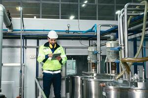 Caucasian technician engineer man in uniform with tablet checking and control boiler tanks and liquid pipeline in production line at factory photo