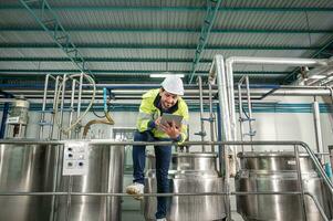 caucásico técnico ingeniero hombre en uniforme con tableta comprobación y controlar caldera tanques y líquido tubería en producción línea a fábrica foto