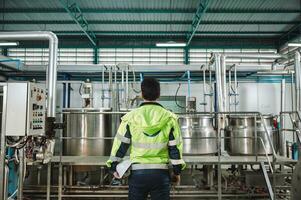 Caucasian technician engineer man in safety uniform standing with pipeline, boiler tank in beverage processing laboratory plant photo