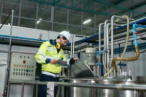 Engineer man in uniform walking to check boiler tanks with liquid pipeline in beverage processing factory photo