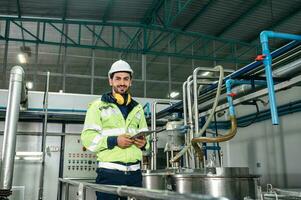 caucásico técnico ingeniero hombre en uniforme con tableta comprobación y controlar caldera tanques y líquido tubería en producción línea a fábrica foto