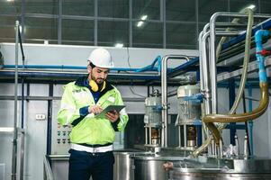 caucásico técnico ingeniero hombre en uniforme con tableta comprobación y controlar caldera tanques y líquido tubería en producción línea a fábrica foto