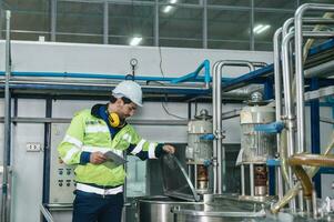 Caucasian technician engineer man in uniform with tablet checking and control boiler tanks and liquid pipeline in chemical factory production line photo