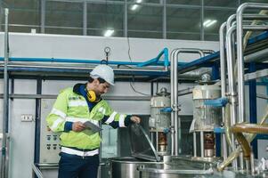 caucásico técnico ingeniero hombre en uniforme con tableta comprobación y controlar caldera tanques y líquido tubería en químico fábrica producción línea foto