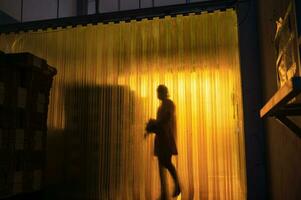 Yellow plastic curtain entrance with shadow of worker and cardboard package in warehouse photo