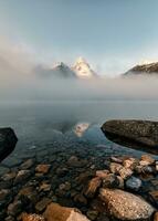 Mount Assiniboine with rocks in foggy on Magog lake in the morning at provincial park photo