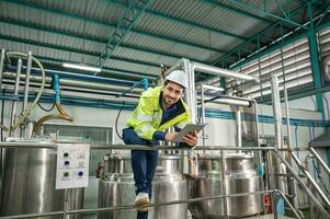 caucásico técnico ingeniero hombre en uniforme con tableta comprobación y controlar caldera tanques y líquido tubería en producción línea a fábrica foto