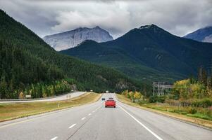 Red car driving on highway with rocky mountains in national park photo