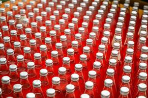 Red juice bottles with screw cap in conveyor belt at beverage processing plant photo