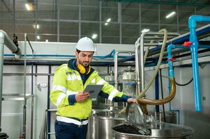 caucásico técnico ingeniero hombre en uniforme con tableta comprobación y controlar caldera tanques y líquido tubería en producción línea a fábrica foto