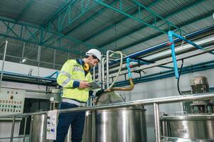 Caucasian technician engineer man in uniform with tablet checking and control boiler tanks and liquid pipeline in chemical factory production line photo