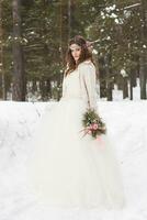 hermosa novia en un blanco vestir con un ramo de flores en un cubierto de nieve invierno bosque. retrato de el novia en naturaleza foto