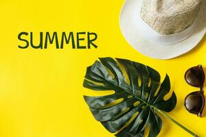 Beach accessories on the yellow background - sunglasses and striped hat. Summer is coming concept.Tropical leaves Monstera. Summer flat lay, top view. Text Summer. photo