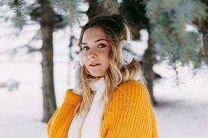 Teen blonde in a yellow sweater outside in winter. A teenage girl on a walk in winter clothes in a snowy forest photo