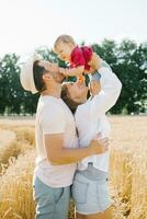 un joven madre, padre y pequeño hijo disfrutar naturaleza juntos en el Fresco aire. un contento familia con un niño camina mediante un trigo campo y disfruta el dulce momentos de su vida foto