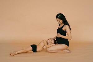 Happy motherhood. A pregnant woman in the studio on a beige background with her five-year-old son photo