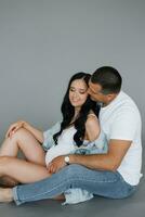 Young happy family husband and wife are expecting a baby. A man embraces a pregnant woman on a gray background photo