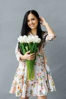 Photo portrait of a brunette girl dreamily holding a bouquet of white tulips in her hands, flowers isolated against a gray background.