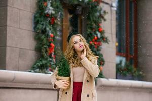 un atractivo contento niña camina alrededor el Navidad invierno ciudad, participación un juguete en su manos foto