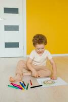 Cute little boy is sitting at home on the floor and drawing a drawing with colored pencils. Child development and creativity for preschoolers and primary school children in kindergarten or at home photo