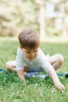 European Caucasian little boy strokes and touches grass and greenery in the forest photo