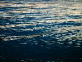 Dark blue sea water surface with dim sunlight reflections. photo