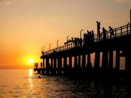 Silhouettes of people jumping into the sea from a wooden pier. photo