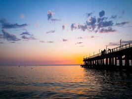 Silhouettes of people jumping into the sea from a wooden pier. photo