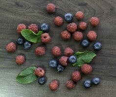 Wild summer berries blueberries and raspberries on wooden background. photo