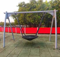 un columpio en un para niños patio de recreo en un público parque, columpio a el patio de recreo en un verano día. para niños columpio hecho de cuerda. equipo para para niños patio de recreo tiene un artificial suave cubierta. foto