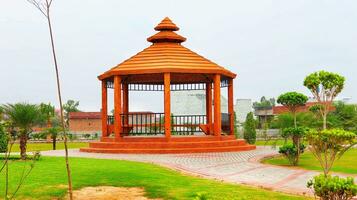 Outdoor Park with shed.Wooden bench in the Park.pavilion garden. green playground .Park with green grass and pedestrian paths for walking,Green grass lawn in front gazebo,palm tree and greenery tree photo