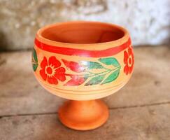 Empty Handmade clay glass water   lay on wood shelf, glass with multiclor flower,clay glass for drinking water ,source natural clay  glass,brown clay water mug photo
