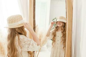 A beautiful teenage girl with long hair measures a straw hat in front of a mirror. Self-admiration of a blonde. photo