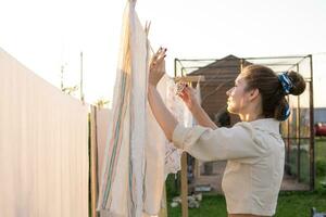 Laundry day. A woman hangs linen and towels on a tree in the courtyard of a village house. photo