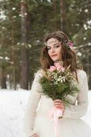 Beautiful bride in a white dress with a bouquet in a snow-covered winter forest. Portrait of the bride in nature photo