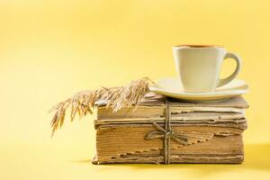 A cup of coffee on old books and dry ears of corn in yellow. Wellness, harmony, quiet reading. Copy space photo
