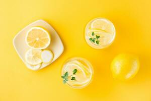 Sparkling water with lemon, melissa and ice in glasses and lemon slices on a saucer on a yellow background. Alcoholic drink hard seltzer. Top view photo