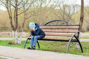 un solitario niña se sienta cubierta su cara con su palmas en un parque banco. mental salud foto