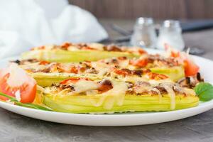 Ready-to-eat baked zucchini halves stuffed with cheese and tomato  on a plate on the table. Vegetable menu, healthy food. Close-up photo