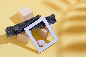 Modern abstract life style background yellow cardboard, blank photo frame, stones, tree bark and shadow from a branch with leaves. Place for text