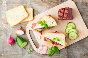 Fresh sandwiches with pastrami, cucumber and radish on a cutting board. American snack. Rustic style. Vertical view. Top view photo