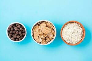 Bowls with different types of breakfasts oatmeal, cereal and chocolate balls on a light blue background. Top view photo