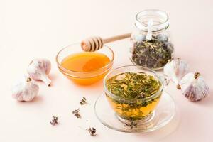 Hot tea with oregano in a cup, honey in a bowl, heads of garlic and dry herb in a jar. Herbal medicine and alternative therapy photo