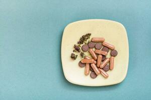 Herbal medicinal capsules, pills and dried oregano on a saucer on a green background. Alternative medicine. Copy space photo