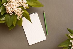 Blank notebook, pencil and bouquets of lilies of the valley on a green background. Top view. Planning, goal setting, wishlist. Spring update photo