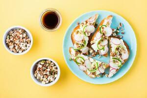 Ready-to-eat bruschetta with curd cheese, vegetables and sprouted grains on a plate on a yellow background. Healthy snacks. Top view photo