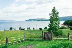 Old abandoned village fence with a gate on a lush meadow on the bank of a Siberian river on a summer day photo